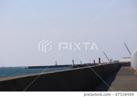 A breakwater along the coast, a jetty with a promenade, a jetty with a lighthouse, a crane, a building, a sea with a blue sea surface, and a landscape of a thin, hazy blue sky. A breakwater along the coast, a jetty with a promenade, a jetty with a lighthouse, a crane, a building, a sea with a blue sea surface, and a landscape of a thin, hazy blue sky. 87526489