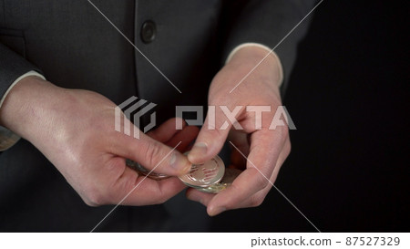 A young businessman in a suit counts crypto currency coins. Hands of a man close-up on a black background. A young businessman in a suit counts crypto currency coins. Hands of a man close-up on a black background. 87527329