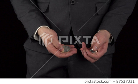 A young businessman in a suit takes out cryptocurrency coins from his pocket and recounts. The waist of a man close-up on a black background. 87527331