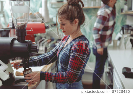 Woman barista working in coffee shop near coffee grinder Woman barista working in coffee shop near coffee grinder 87528420