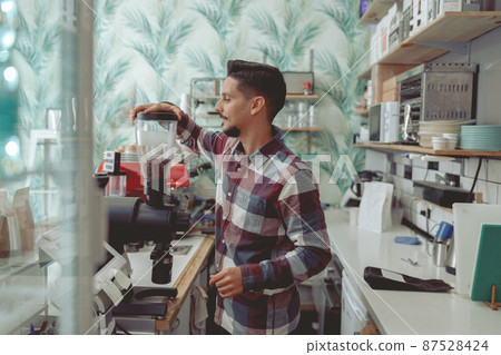 Portrait of man barista grinding coffee beans Portrait of man barista grinding coffee beans 87528424