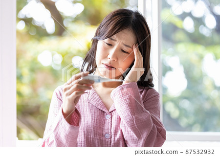 A woman in a room wear who looks negative when she sees the thermometer in her hand 87532932