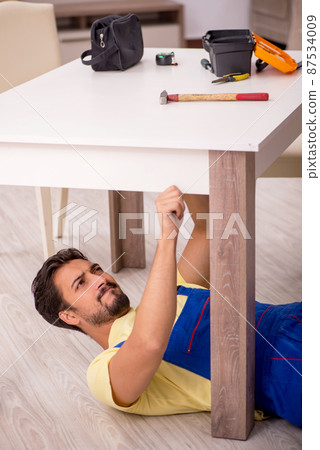 Young male carpenter repairing table at home 87534009