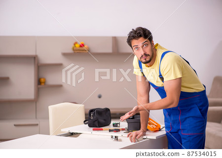 Young male carpenter repairing table at home 87534015