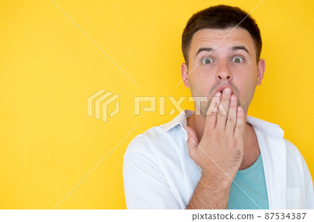 Unbelievable situation. Amazed man. Disbelief face. Shocked guy wide opened eyes covering mouth with hand isolated yellow copy space. 87534387