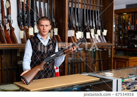 Portrait of an arms shop salesman with pump-action shotgun in hands 87534958