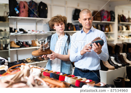 Shoe salesman helping teen to choose fashionable winter boots at shoe shop 87534960