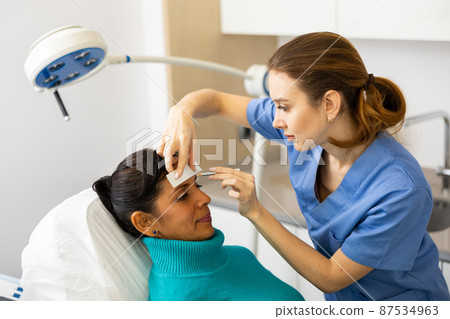 Beautician using white pencil and ruler for marking skin of latin woman 87534963