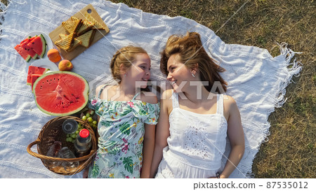 Happy mother touches daughter nose lying on picnic blanket 87535012