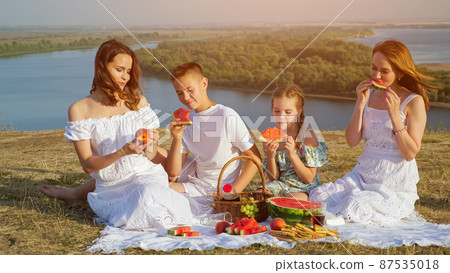 Mother and happy children have festive picnic on green hill Mother and happy children have festive picnic on green hill 87535018