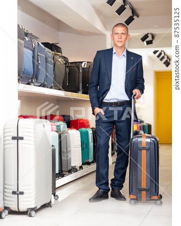 Positive man chose suitcase in haberdashery store 87535125