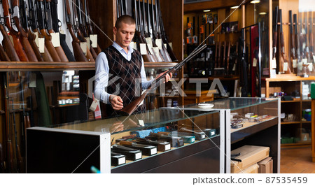 Adult owner of the gun shop demonstrates rare collectible hunting rifle 87535459