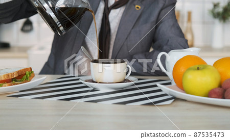 Close-up of Man Entrepreneur Pouring Coffee while Having Breakfast at Home. Coffee Spills over the Rim of the Cup. Business, Lifestyle, Overworking Concept Close-up of Man Entrepreneur Pouring Coffee while Having Breakfast at Home. Coffee Spills over the Rim of the Cup. Business, Lifestyle, Overworking Concept 87535473