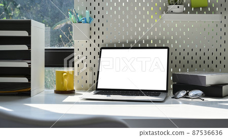 Computer laptop, coffee cup and supplies on white table in bright home office. Computer laptop, coffee cup and supplies on white table in bright home office. 87536636