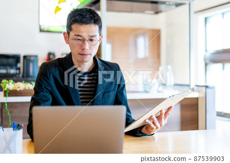 一位男性企業家，他檢查印刷材料的內容並在計算機上進行更正 87539903