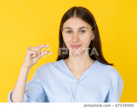 Small size. Pretty woman. Measurement gesture. Smiling cute brunette lady showing fingers sign of little bit isolated yellow. 87539998