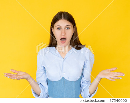 Shocked woman. Unexpected situation. Unsure emotion. Embarrassed pretty lady shrugging hands looking clueless isolated yellow. 87540000