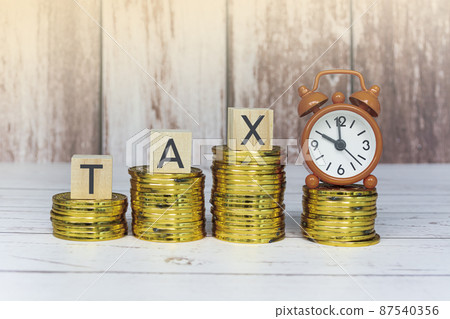 Tax text on wooden blocks and alarm clock set at 10 o'clock with gold coins. 87540356