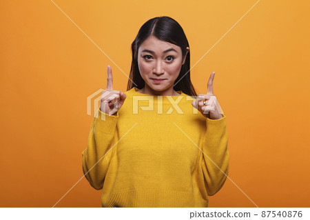 Confident woman pointing index fingers overhead while looking at camera Confident woman pointing index fingers overhead while looking at camera 87540876