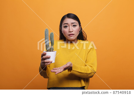 Confused uncertain asian woman gesturing unsurely while holding cactus plant. Confused uncertain asian woman gesturing unsurely while holding cactus plant. 87540918