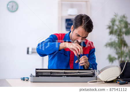 Young male repairman repairing air-conditioner Young male repairman repairing air-conditioner 87541112