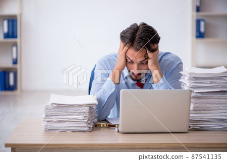 Young male employee and too much work in the office Young male employee and too much work in the office 87541135