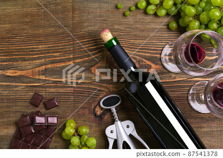 Red wine bottle, grape, chocolate and glasses over wooden table. Top view with copy space 87541378