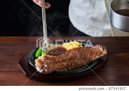 A cook who puts sauce on hot loin steak 87541937