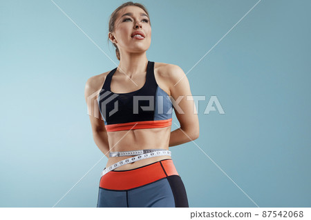 Fit fitness girl measuring her waistline with measure tape. Weight loss, slim body, healthy lifestyle concept. 87542068