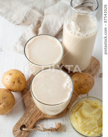 Potato milk pouring into glass on white wooden bg 87543026
