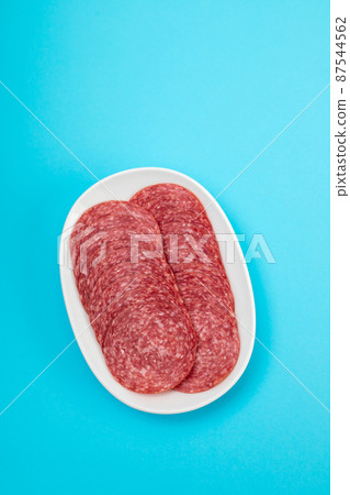 fresh cut salami on small white plate on blue fresh cut salami on small white plate on blue 87544562