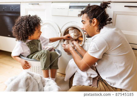 Son helping dad to load washing machine Son helping dad to load washing machine 87545185