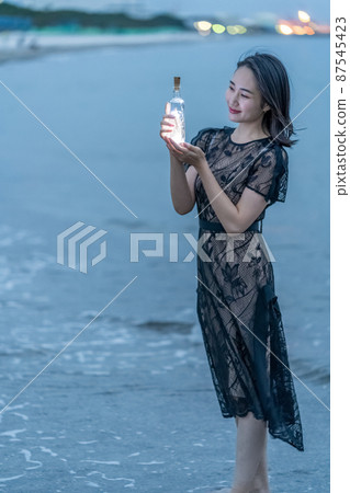 Coastal woman traveling alone evening view magic hour memory bottle mail Coastal woman traveling alone evening view magic hour memory bottle mail 87545423