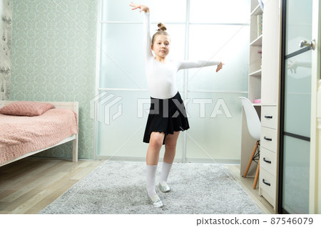 A child in a white gymnastic leotard is dancing at home, distance learning dance. Dance classes at home A child in a white gymnastic leotard is dancing at home, distance learning dance. Dance classes at home 87546079