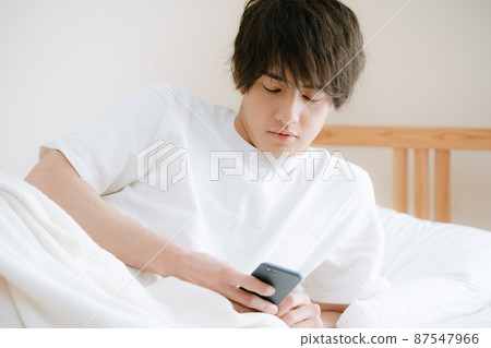 Young man watching smartphone in bed Young man watching smartphone in bed 87547966