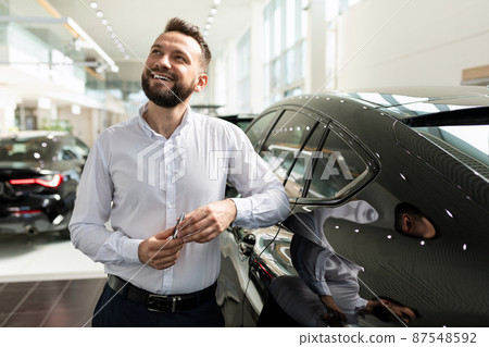 a man in a car dealership dreaming about a new car with a smile on his face 87548592