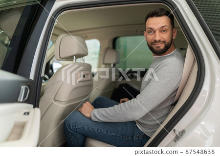 a customer in a car dealership sits in the back seat of a car with a smile on his face a customer in a car dealership sits in the back seat of a car with a smile on his face 87548638