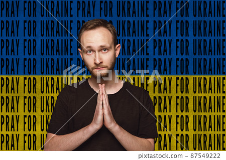Portrait of Ukrainian man praying for Ukrainian safety isolated over blue and yellow flag background with lettering Pray for Ukraine Portrait of Ukrainian man praying for Ukrainian safety isolated over blue and yellow flag background with lettering Pray for Ukraine 87549222