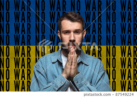 Portrait of Ukrainian man crying and praying for Ukrainian safety and peace isolated over blue and yellow flag with lettering No war Portrait of Ukrainian man crying and praying for Ukrainian safety and peace isolated over blue and yellow flag with lettering No war 87549224