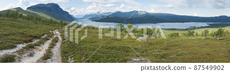 Panoramic landscape with beautiful river Lulealven, snow capped mountain, birch trees and two hikers couple at Kungsleden hiking trail near Saltoluokta, Sweden, Lapland wild nature. Summer blue sky 87549902