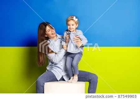 Portrait of young woman, mother with her little girl, daughter isolated over blue and yellow Ukrainian flag background 87549903