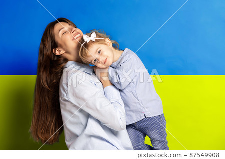 Portrait of young woman, mother with her little girl, daughter isolated over blue and yellow Ukrainian flag background. No war Portrait of young woman, mother with her little girl, daughter isolated over blue and yellow Ukrainian flag background. No war 87549908