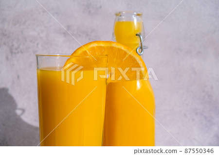 Glass of fresh squeezing Orange juice with sliced fruits on concrete background. Fruit juice, fresh cold drink. Refreshment in summer. Fruits cut in half Glass of fresh squeezing Orange juice with sliced fruits on concrete background. Fruit juice, fresh cold drink. Refreshment in summer. Fruits cut in half 87550346