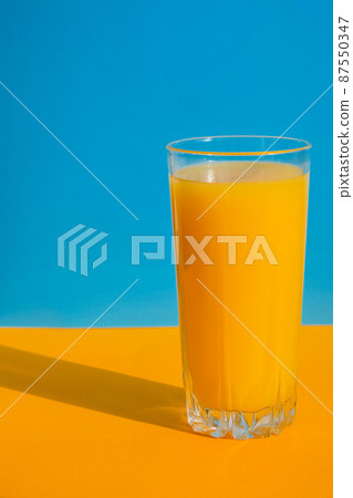 Glass of fresh squeezing Orange juice on blue and yellow background. Fruit juice, fresh cold drink. Refreshment in summer. Glass of fresh squeezing Orange juice on blue and yellow background. Fruit juice, fresh cold drink. Refreshment in summer. 87550347