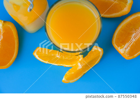 Glass bottle of fresh squeezing Orange juice with sliced fruits on blue background. Fruit juice, fresh cold drink. Refreshment in summer. Fruits cut in half Glass bottle of fresh squeezing Orange juice with sliced fruits on blue background. Fruit juice, fresh cold drink. Refreshment in summer. Fruits cut in half 87550348