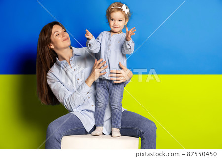 Portrait of young woman, mother with her little girl, daughter isolated over blue and yellow Ukrainian flag background. Free Ukraine Portrait of young woman, mother with her little girl, daughter isolated over blue and yellow Ukrainian flag background. Free Ukraine 87550450