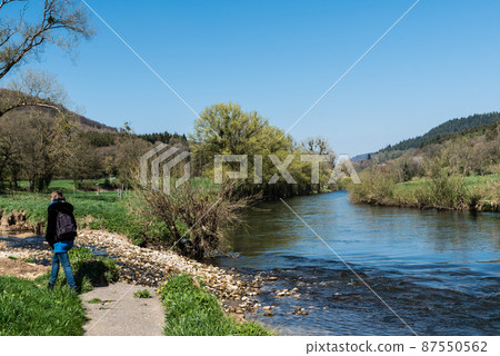 Woman with small backpack on a walking trail along the banks of the Sauer river Woman with small backpack on a walking trail along the banks of the Sauer river 87550562