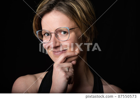 Low key studio portrait of a 35 year old white woman, chin resting on hands, playful 87550573