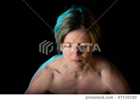 Low key studio portrait of a 35 year old white woman with naked shoulders, showing her muscled chest 87550580