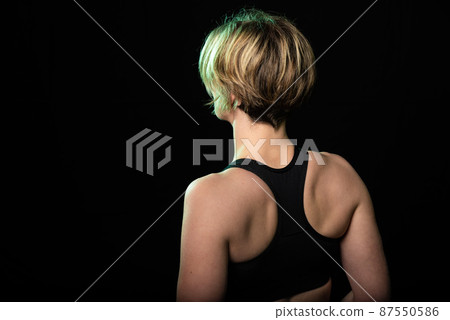 Low key studio portrait of a 35 year old white woman showing her back in a fitness top 87550586